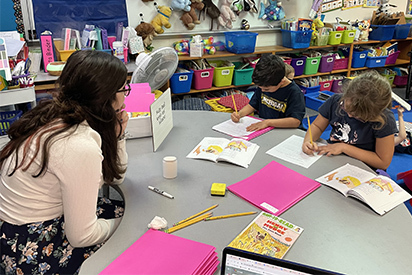 A Teacher Academy student helps local school children with a writing assignment